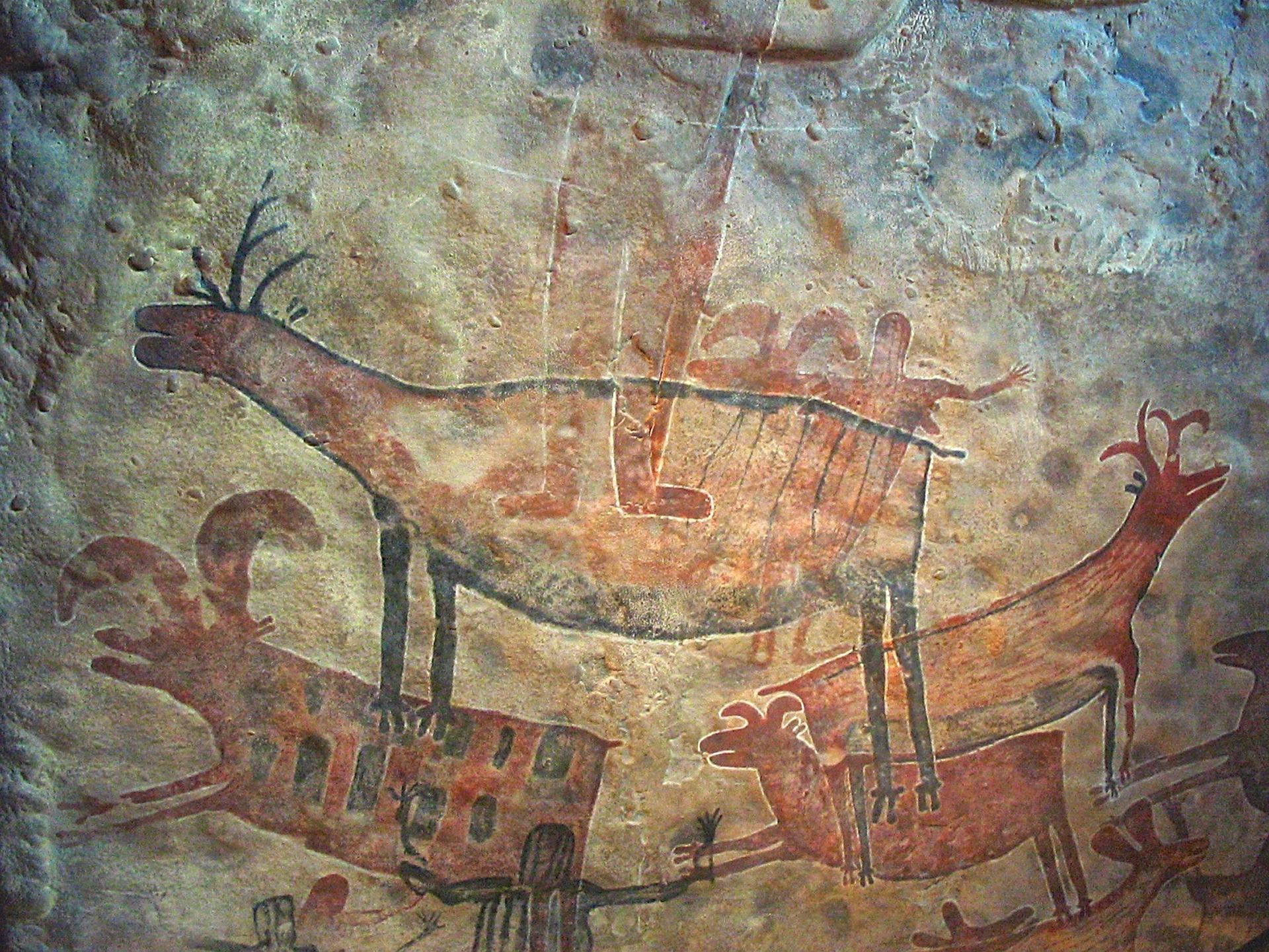 Cave painting of reddish-brown animals, possibly deer, on a light-colored rock surface.