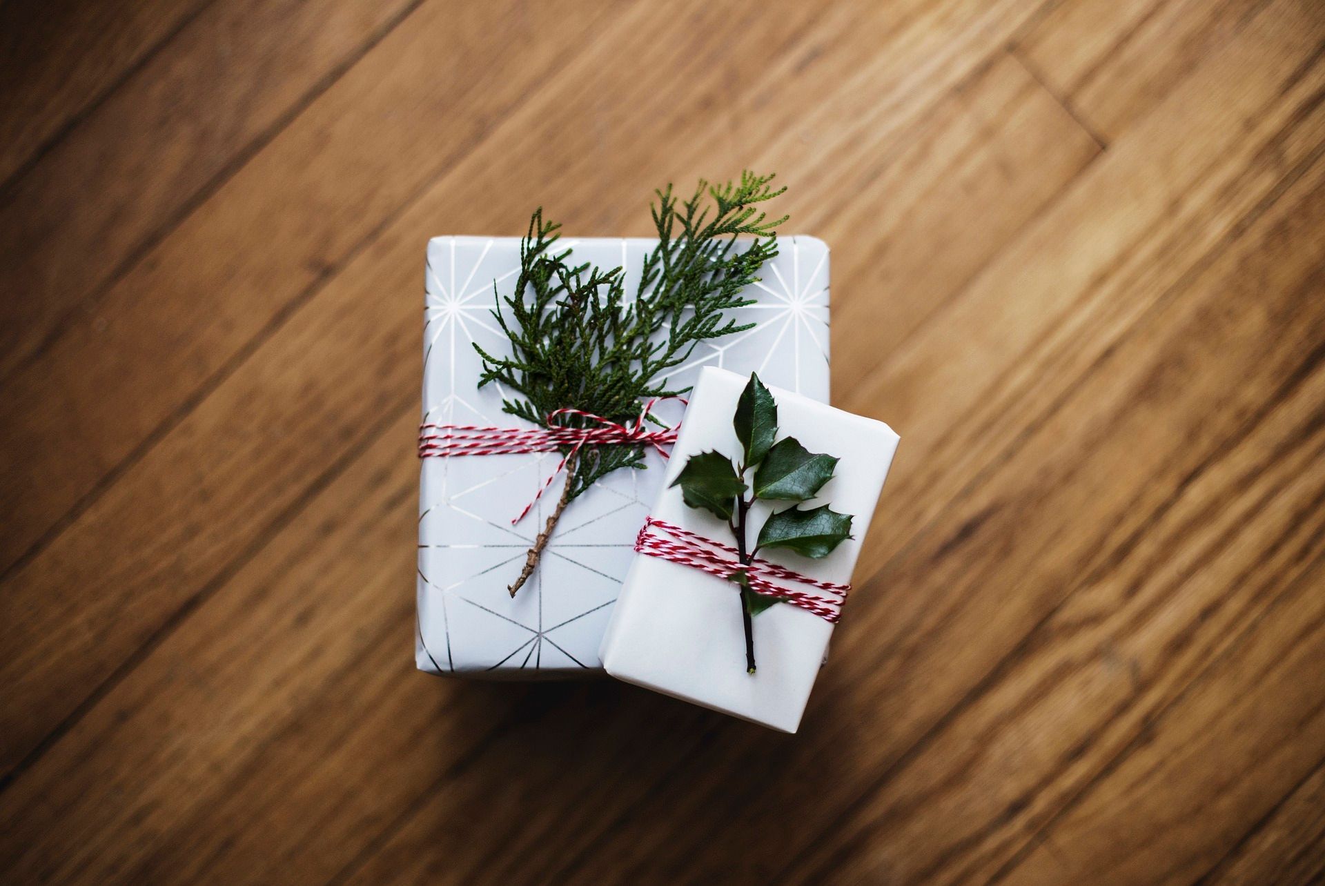Two wrapped gifts on wooden floor, decorated with greenery and red twine.