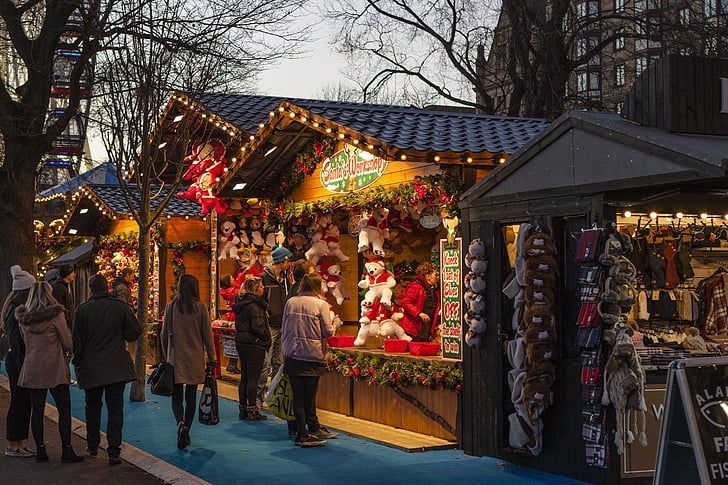 Christmas market stalls with lights, shoppers browsing festive goods.