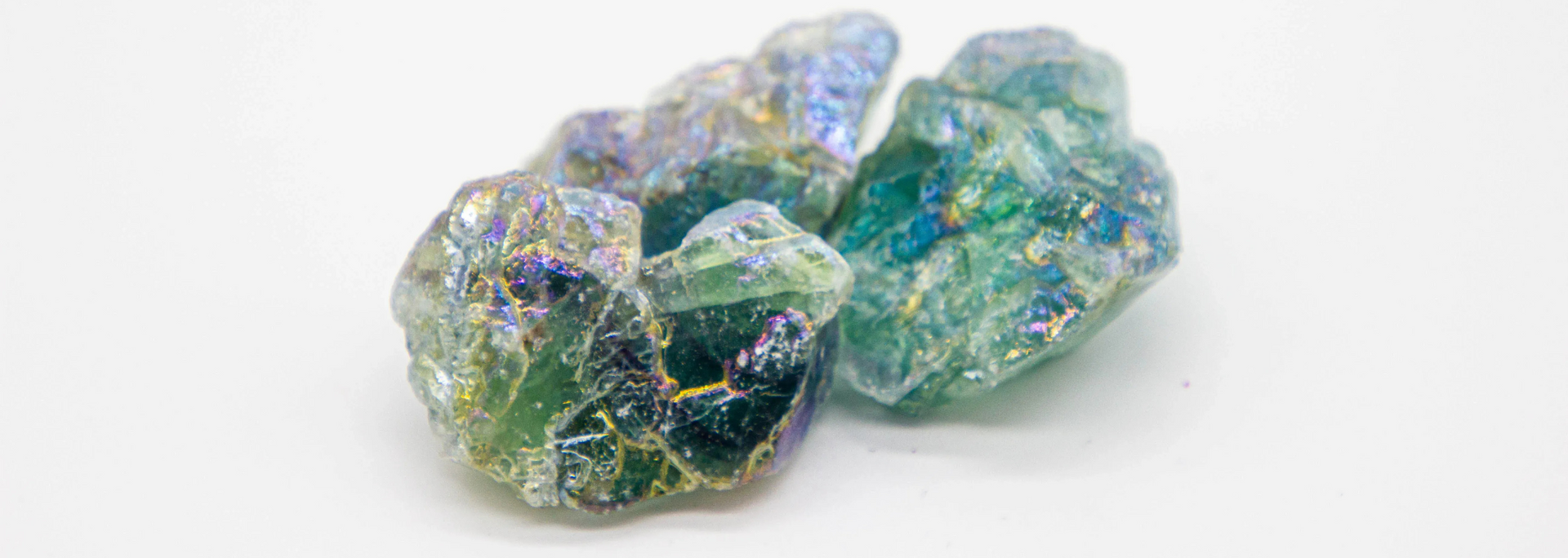 Close-up of three iridescent green and blue crystals on a white surface.