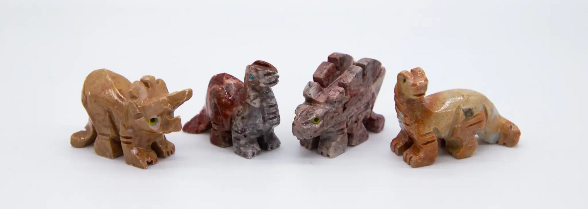 Four stone dinosaur figurines on a white background.