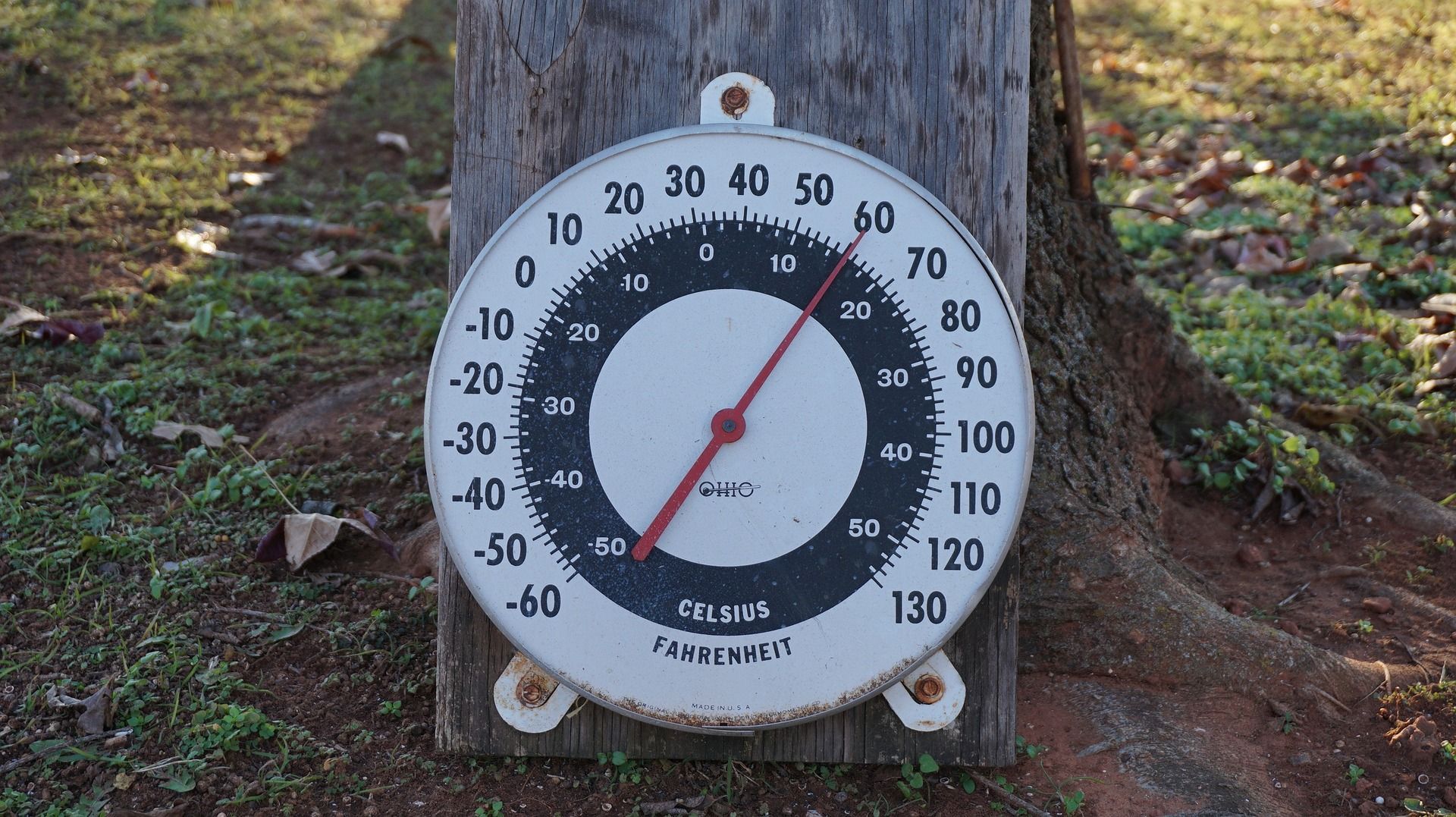 Outdoor thermometer attached to a wooden post, measuring approximately 68 degrees Fahrenheit.
