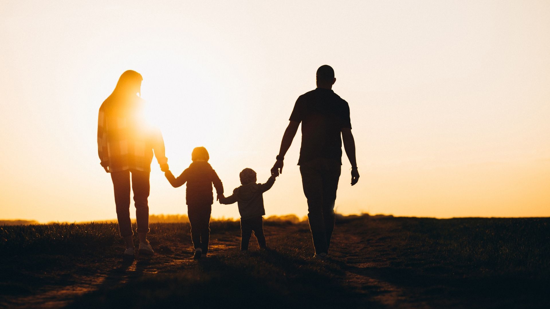 Family of four walking hand-in-hand toward setting sun.