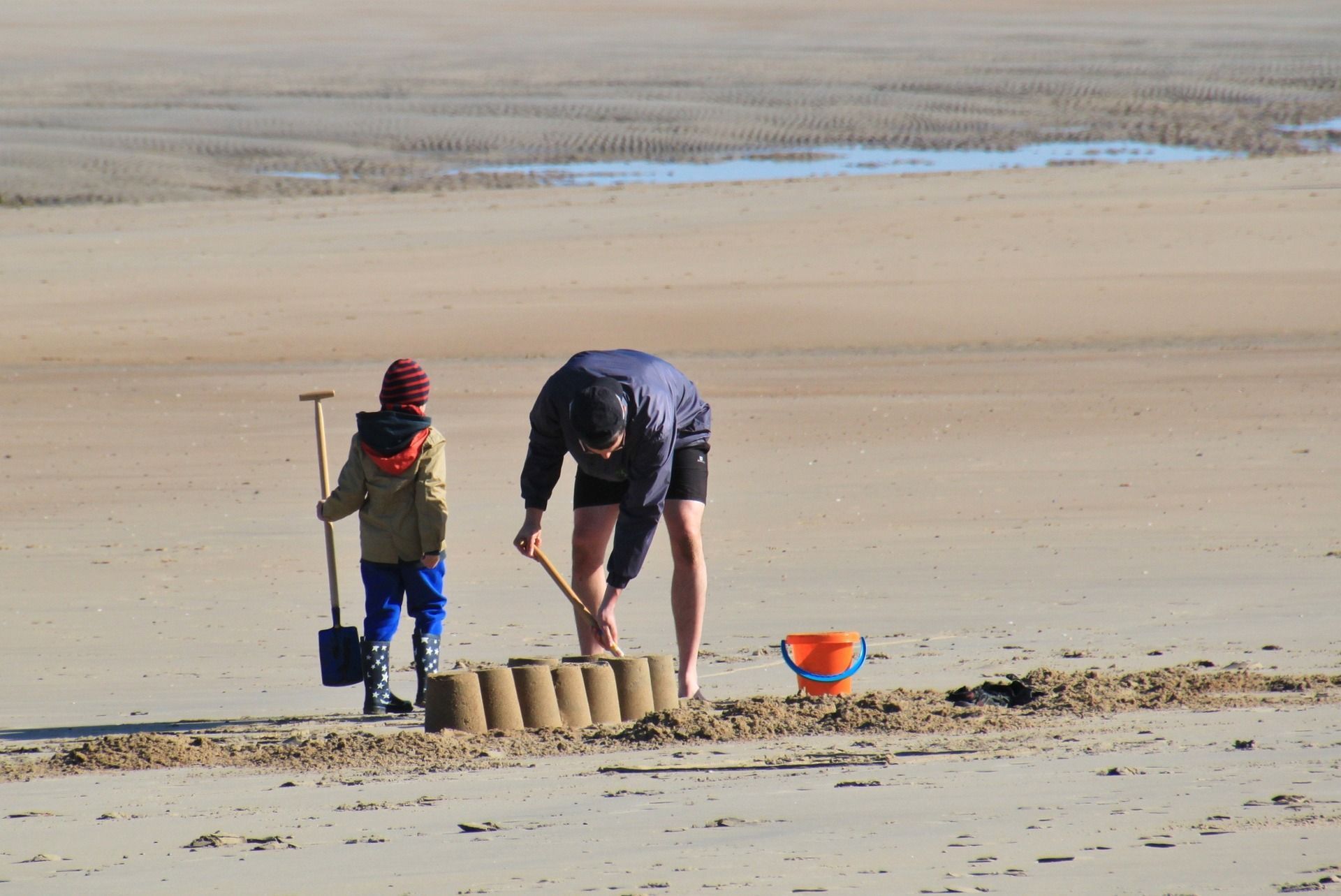 Father and child building sandcastle wall on beach, sunny day.