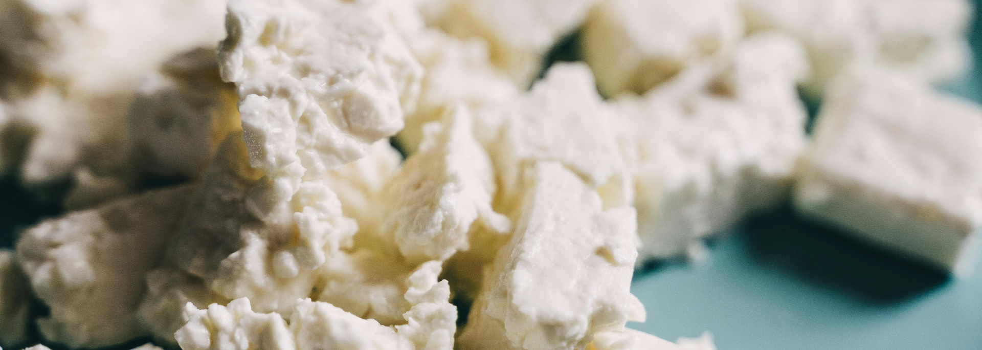 Close-up of white, crumbly cheese cubes on a pale blue surface.