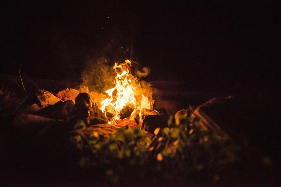 Campfire burning brightly at night, surrounded by rocks and foliage.