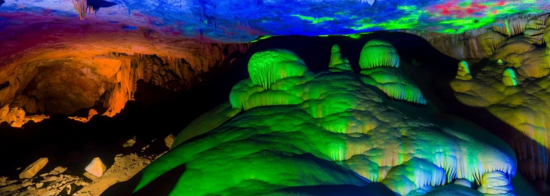 A vibrantly lit cave with green, blue, and orange rock formations.