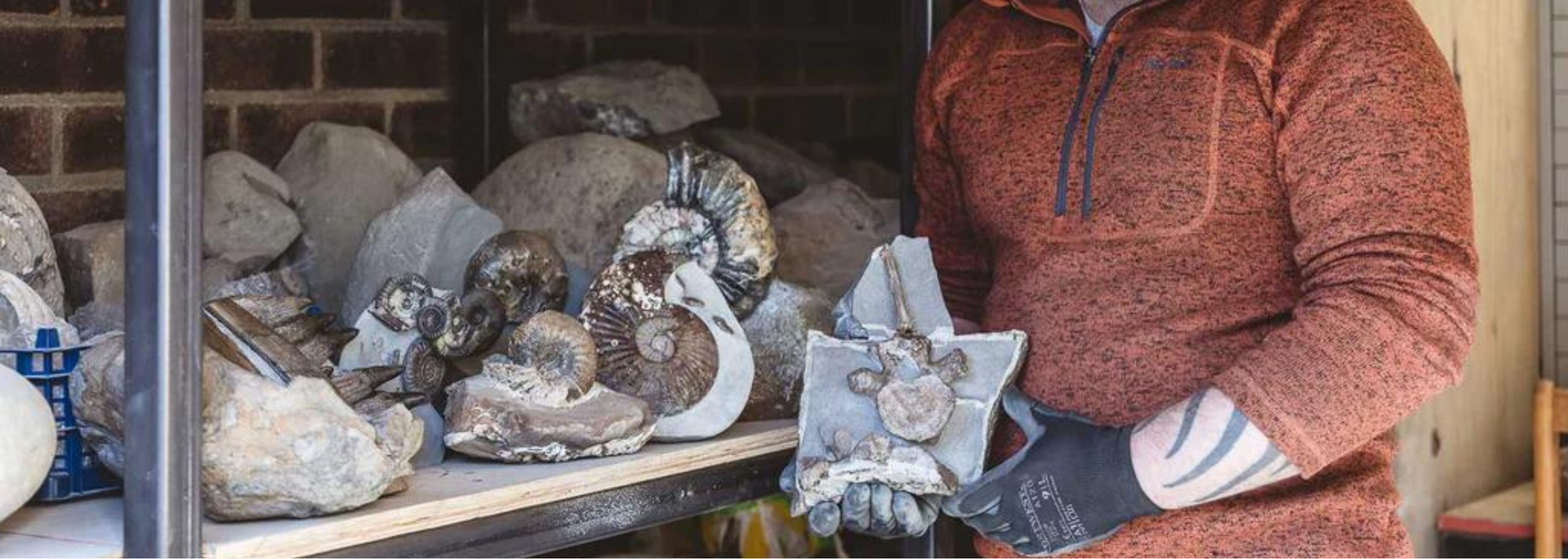 Person in rust-colored sweater holding a sculpture. Many more sculptures sit on shelves in a brick-walled room.
