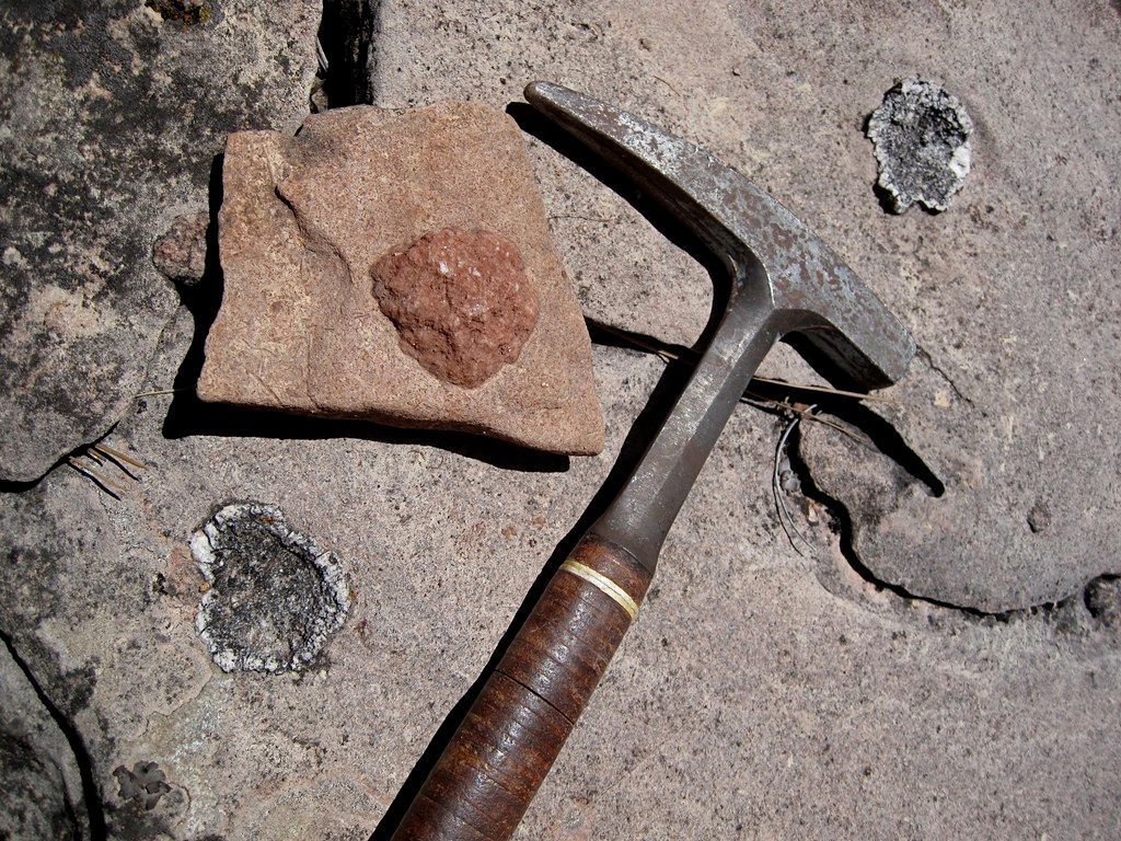 Rock sample with embedded stone next to a geological hammer on a cracked surface.