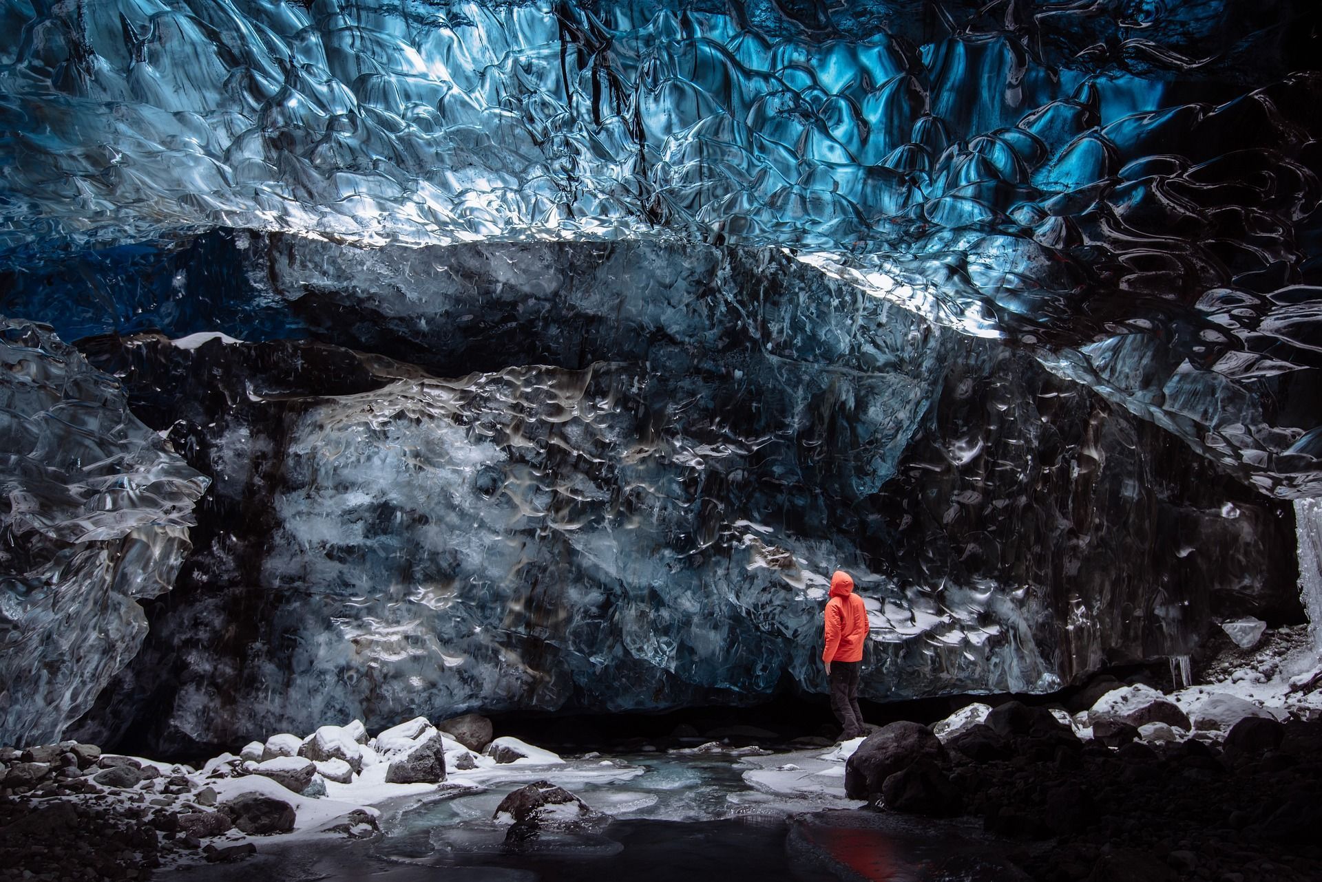 Person in orange coat stands in an icy blue cave.
