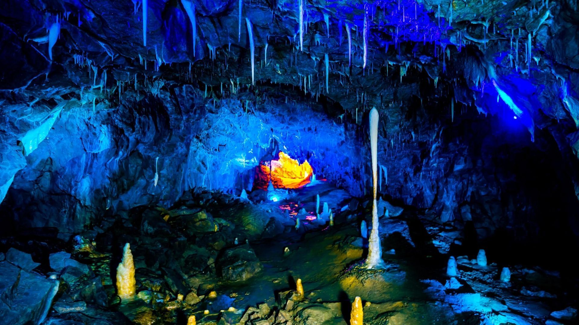 Cave illuminated with blue and orange lights, featuring stalactites and stalagmites.