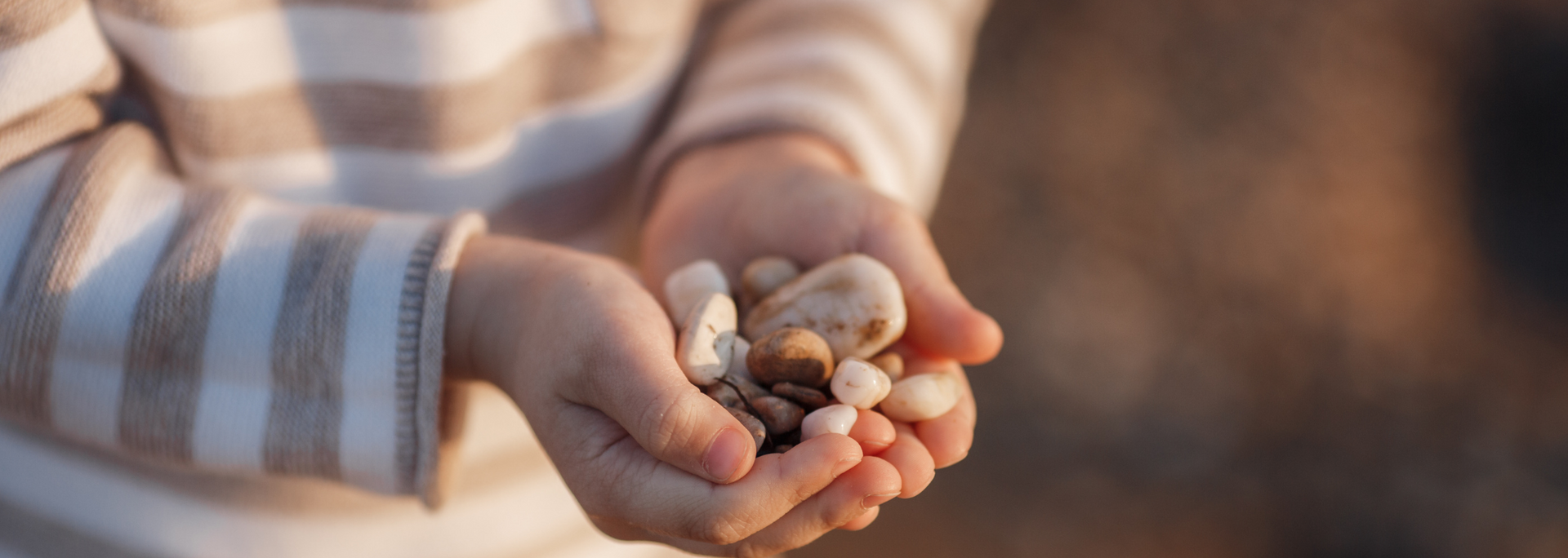 Child's hands holding a handful of smooth, colorful pebbles. A striped sleeve is visible.