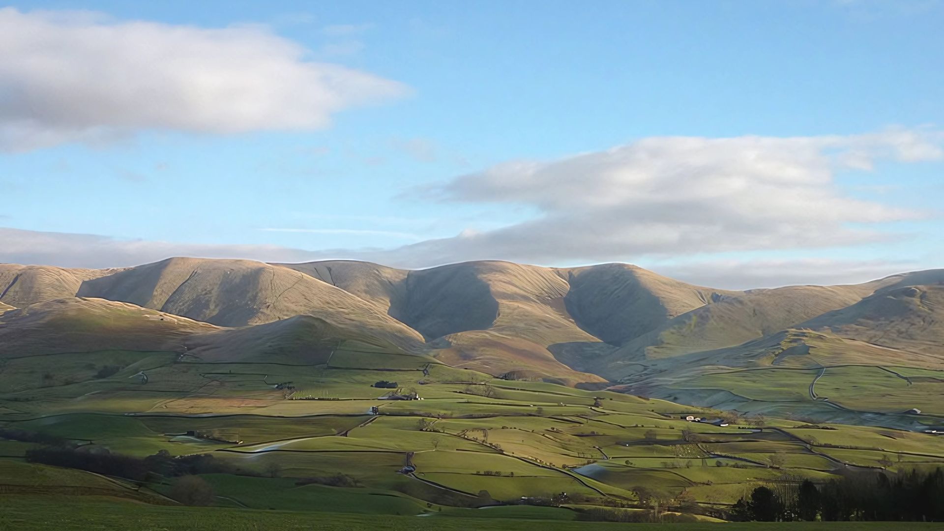 Rolling hills and green fields under a blue sky with scattered clouds.