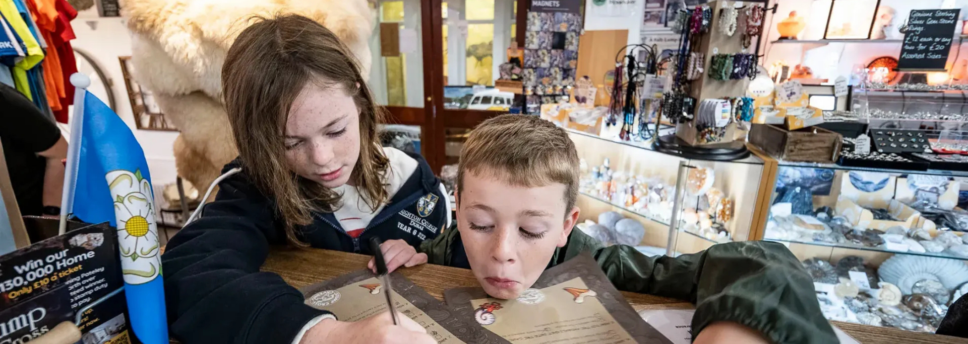 Two children examining an old map at a shop counter, with a blurred background of merchandise.