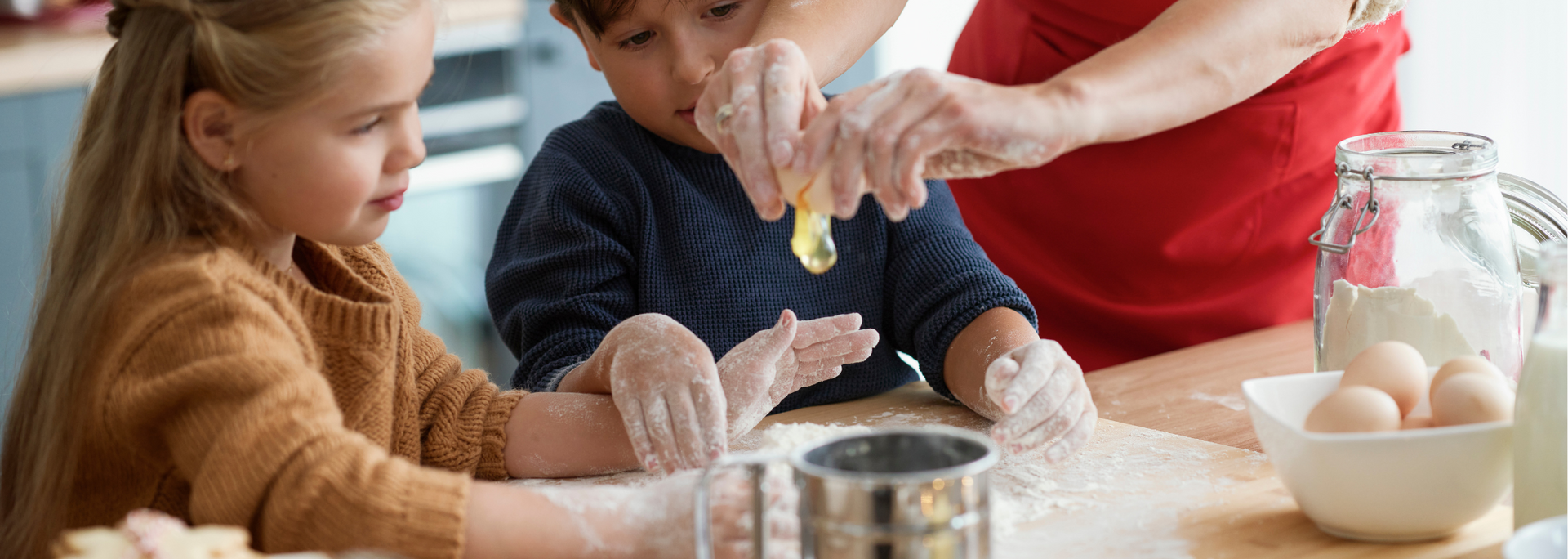 Children and adult baking together in a kitchen. Flour covers the table and their hands.