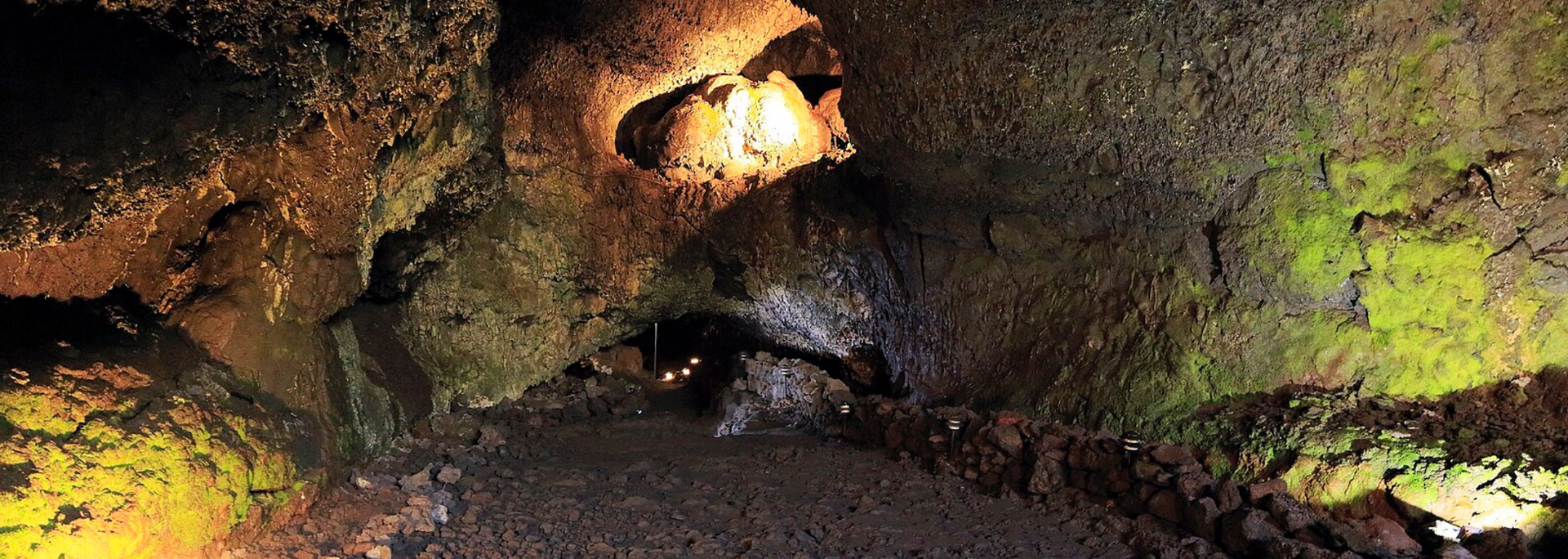 Inside a dark cave, with rough, textured walls lit by amber and green light.