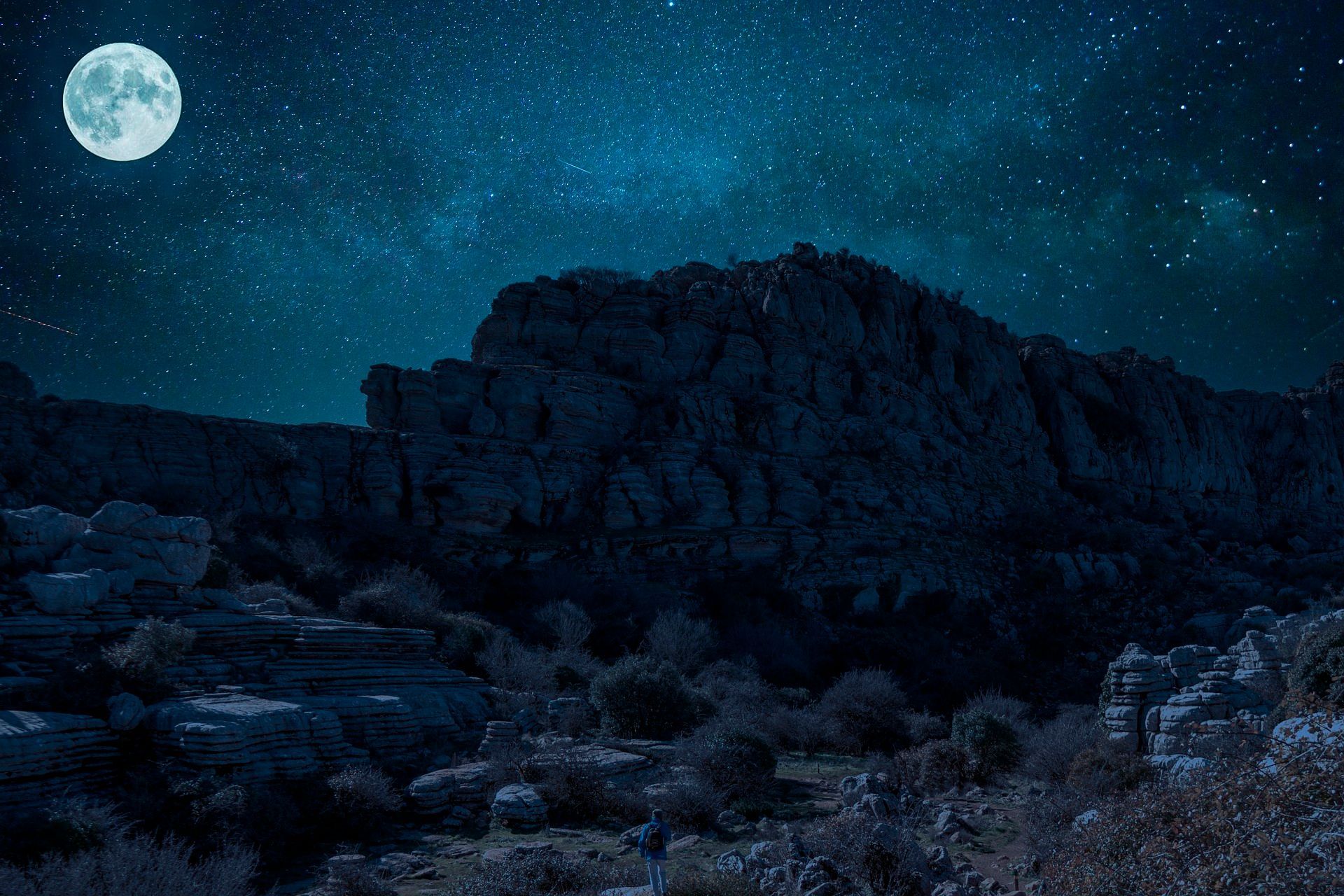 Full moon over dark, rocky mountains and starry night sky.