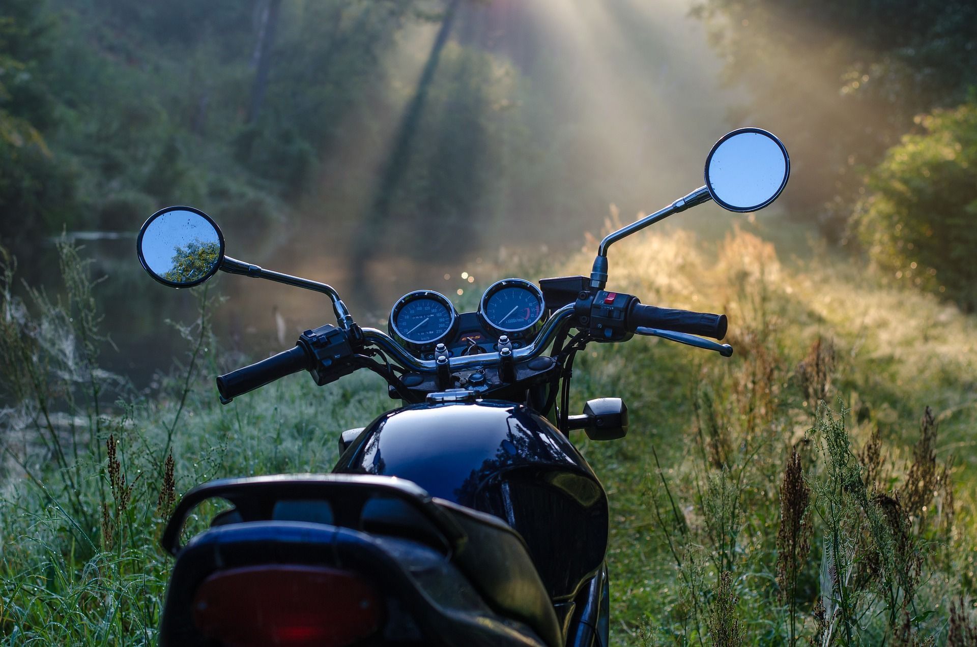 Motorcycle parked in a misty forest, sun rays shining.