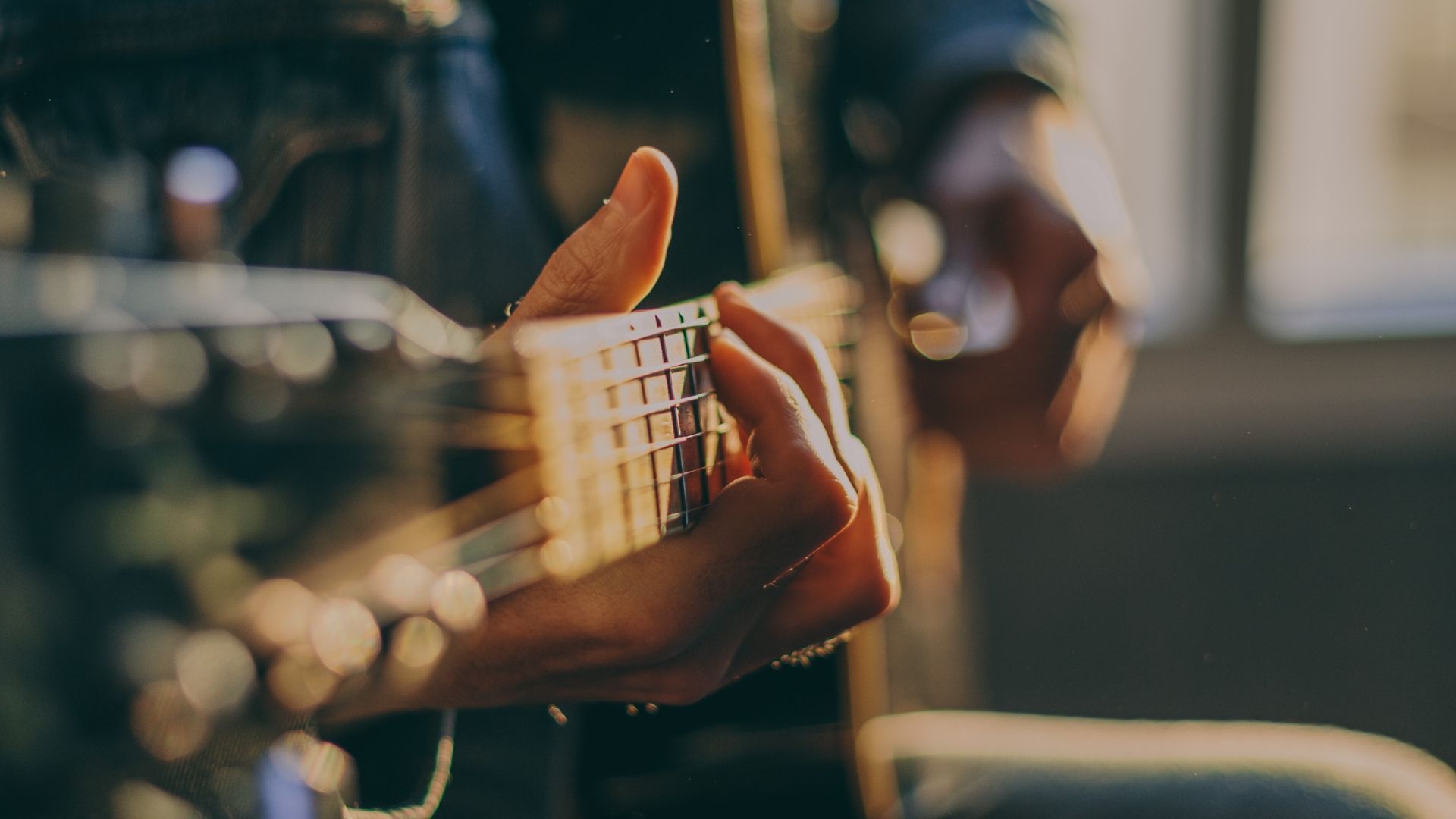 Close-up of a person's hands playing an acoustic guitar. Focus on fretting hand pressing down on strings.