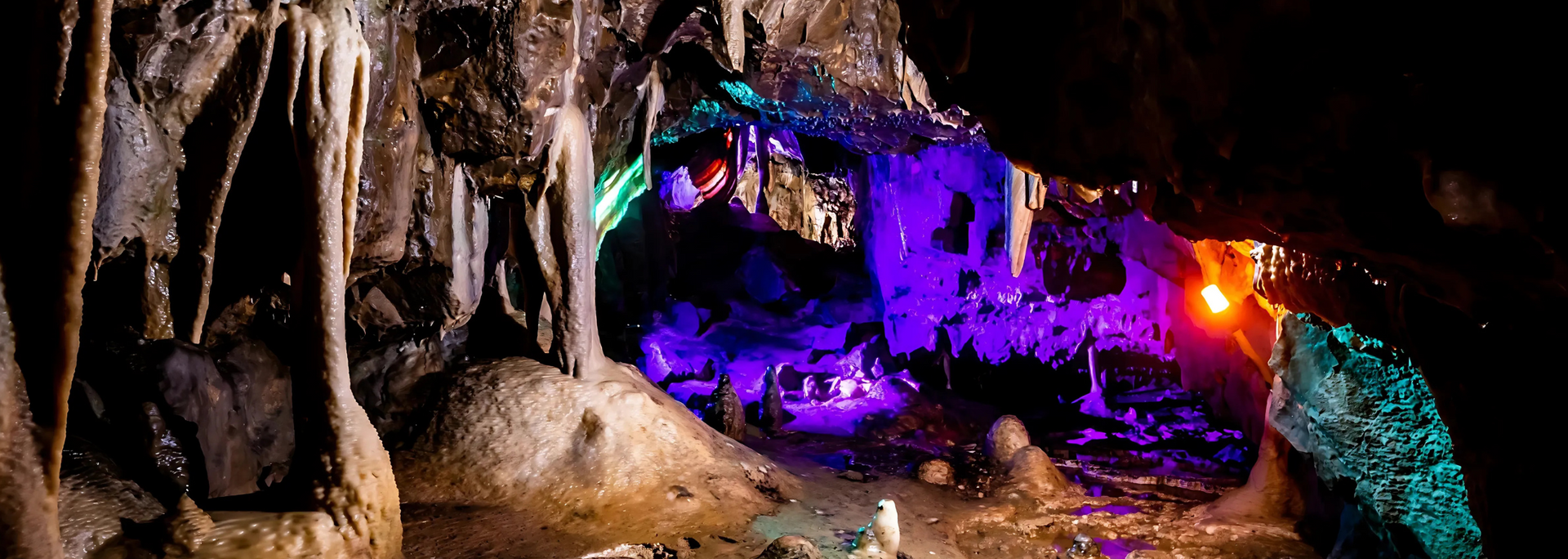 A cave interior with colorful lighting, including purple, green, and orange, illuminating rock formations.