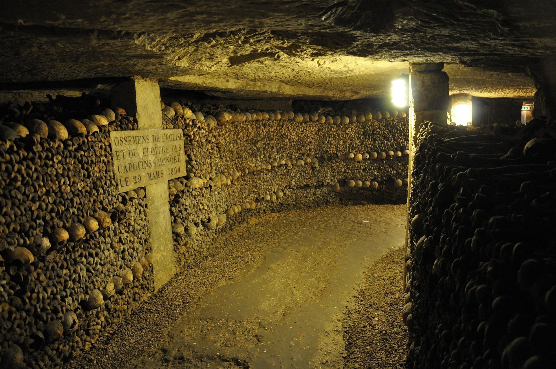 Interior of the Paris Catacombs, tunnels lined with skulls and bones, a sign visible.