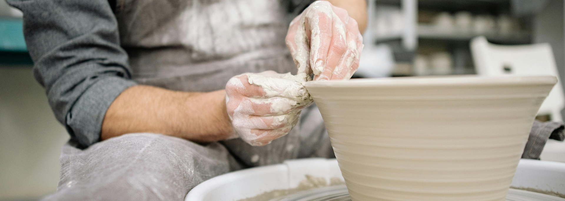 Person covered in clay making a bowl on a pottery wheel.