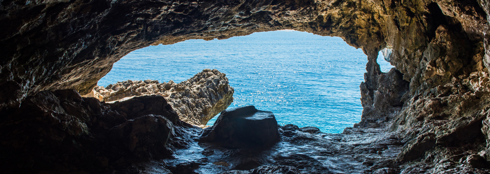 A cave opening frames a view of blue ocean water. Rocky cave walls surround the view.