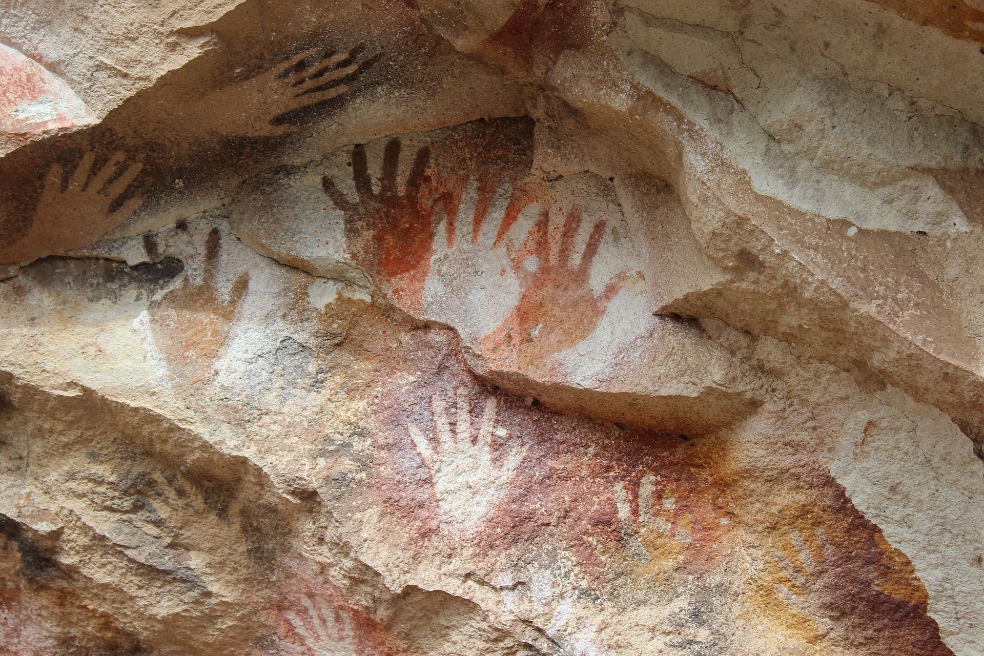 Rock art: red and black handprints on a beige, textured surface.