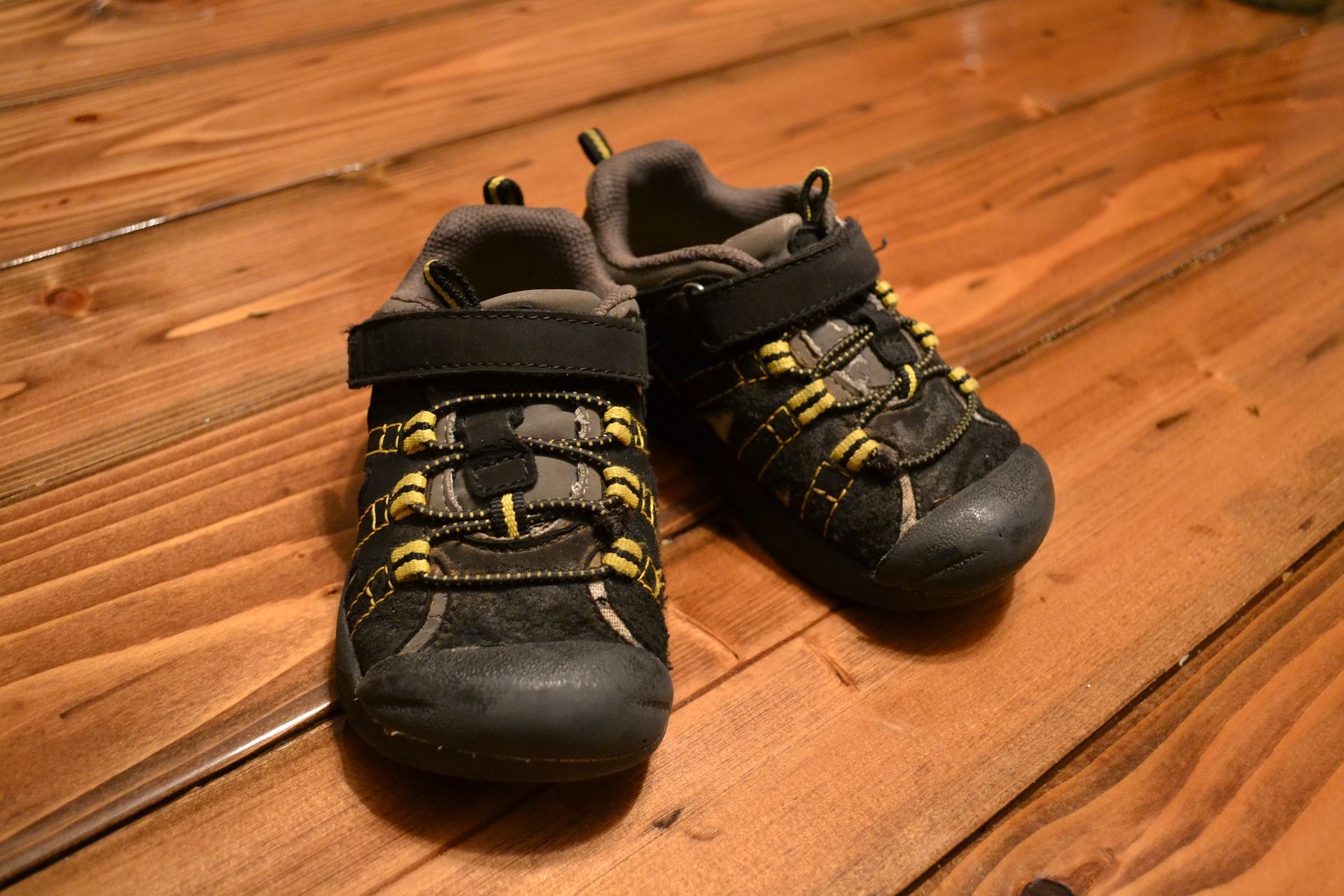 Pair of black and gray children's shoes with yellow laces, on a wooden floor.