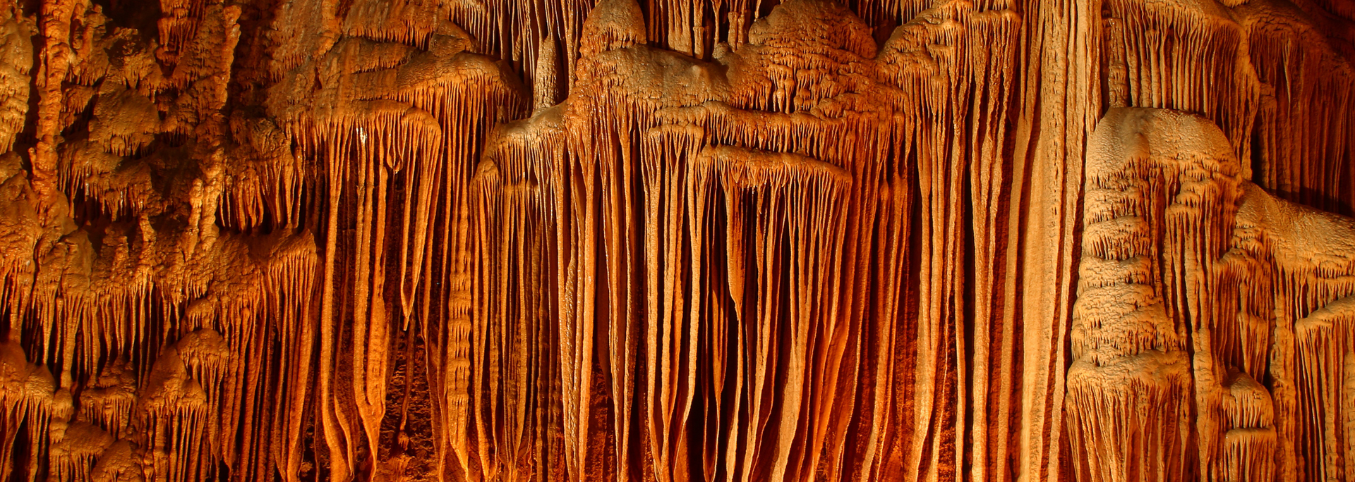Cave formation with long, textured, brown stalactites hanging from the ceiling.