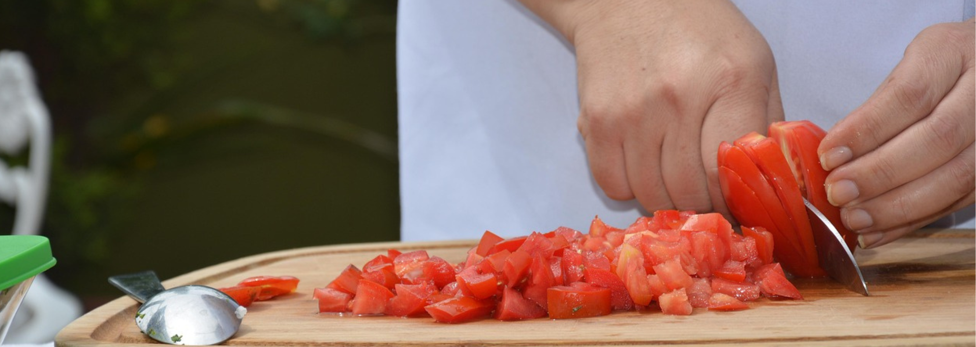Person slicing a red tomato on a wooden cutting board, with diced tomatoes visible.