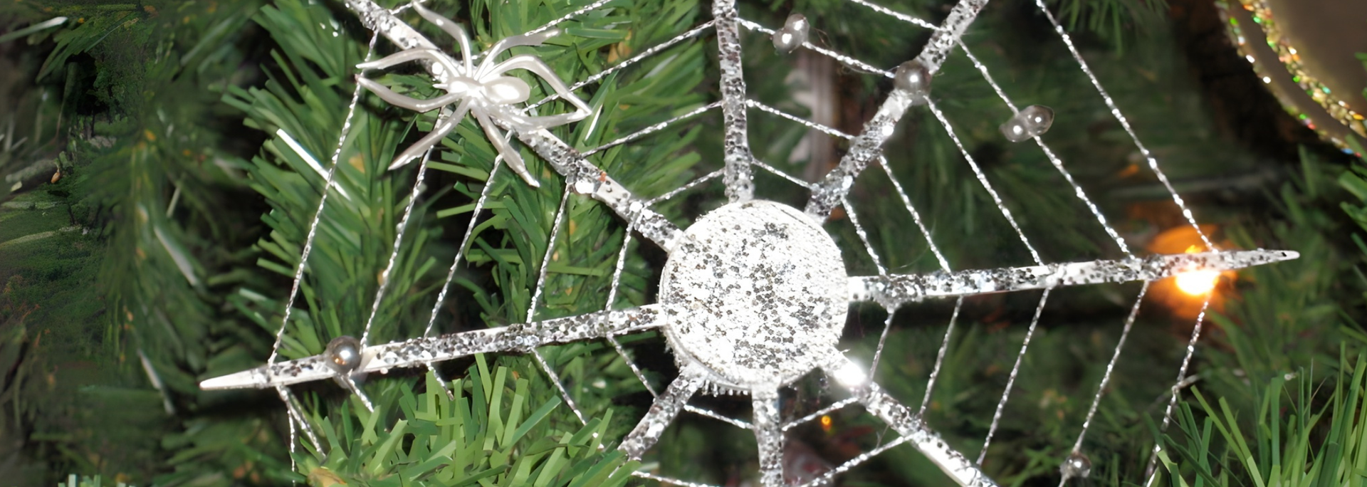 A sparkly spider web ornament with a spider rests on a green tree.