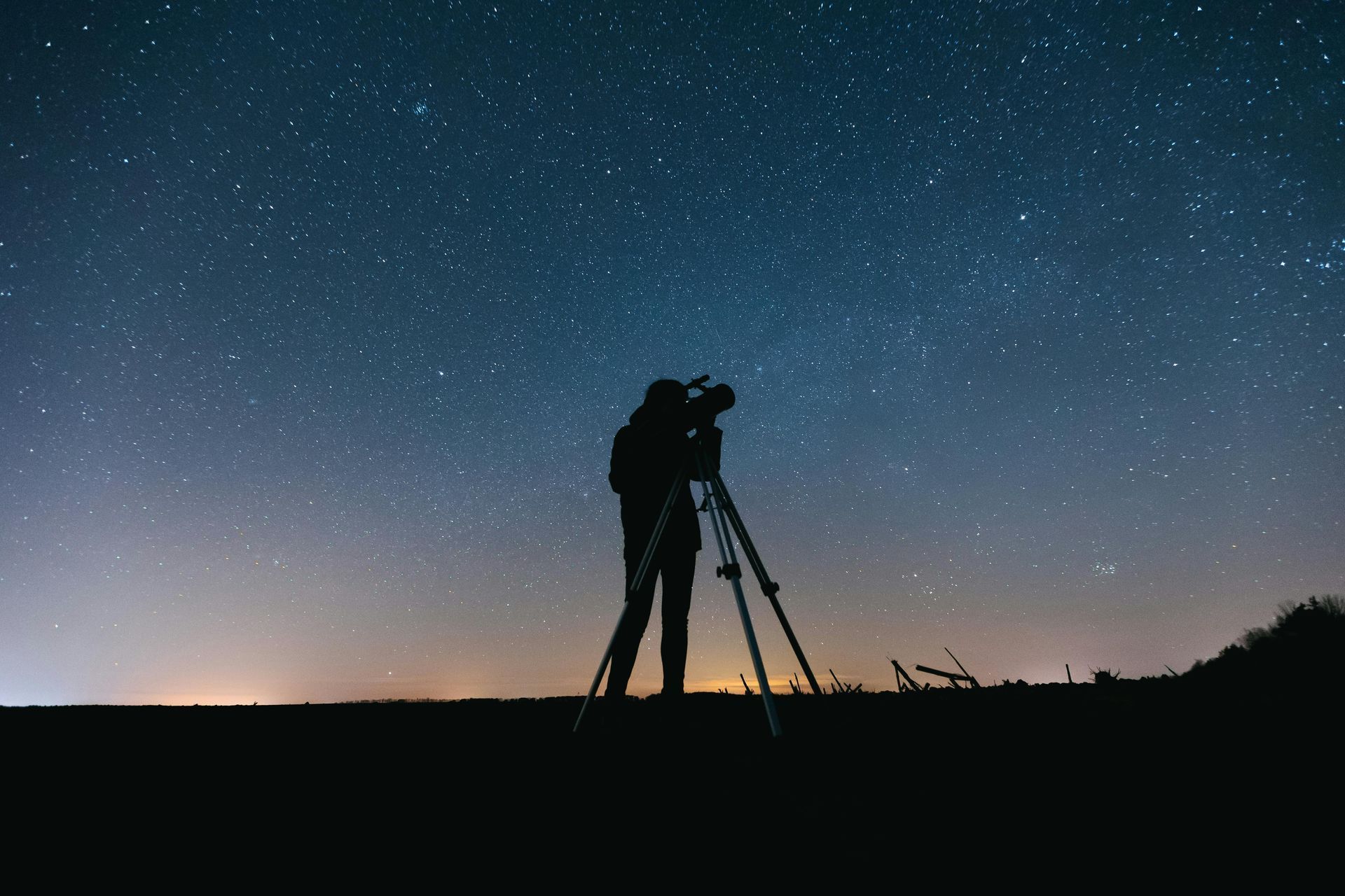 Silhouette of person with a telescope, observing starry night sky.
