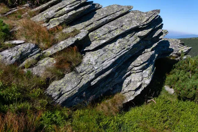 Layered gray rock formation in a grassy, sunny landscape.