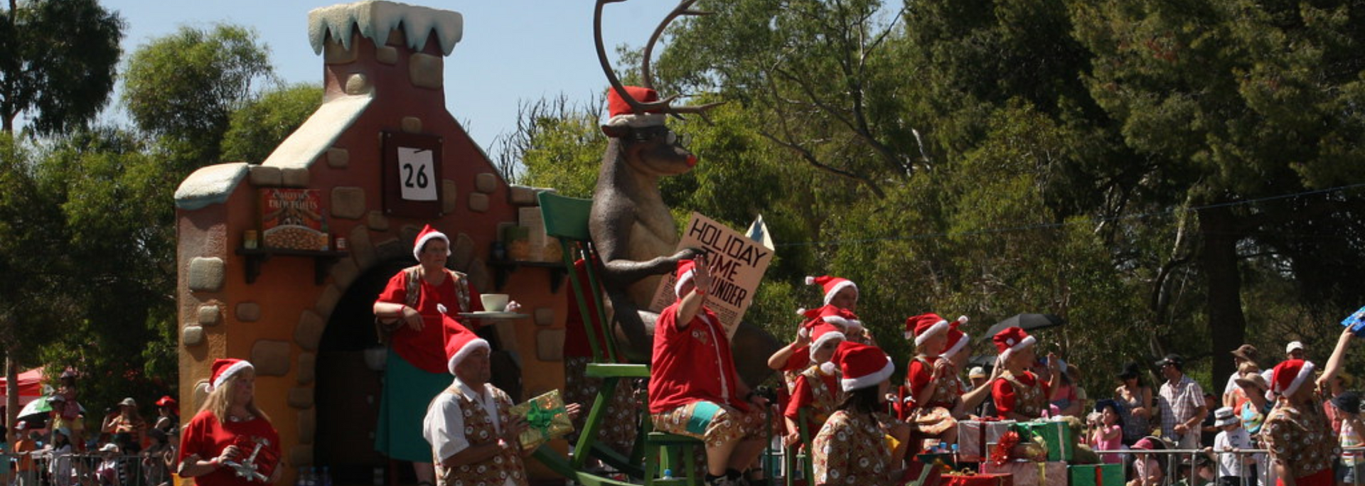 Christmas parade float with reindeer, castle, and people in Santa hats.