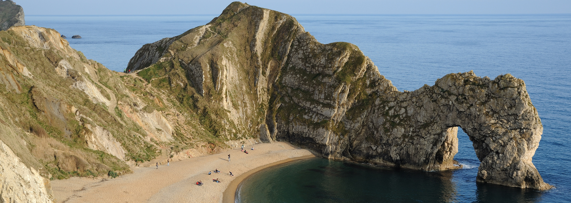 Coastal scene with a large rock arch and beach along the English Channel.