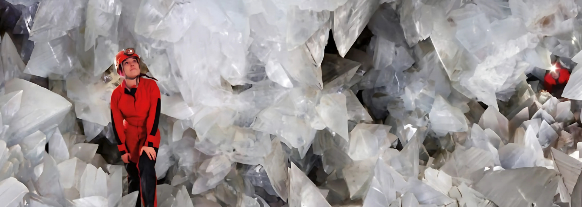 Person in red suit explores a cave filled with giant, translucent gypsum crystals.