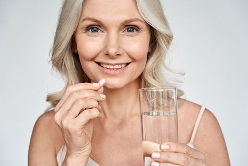 Woman holding a pill and a glass of water, smiling at the camera.