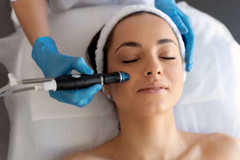 Woman receiving facial treatment; therapist in blue gloves holds a tool to her face.