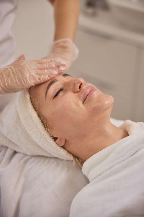 Woman receiving a facial treatment with hands applying product to her face, eyes closed.