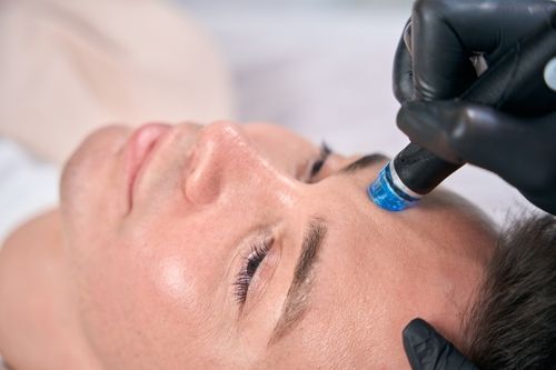 Person receiving facial treatment with blue handheld device on forehead.