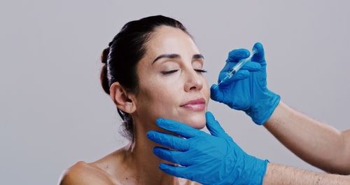 Woman receiving facial injection with blue-gloved hands, light background.