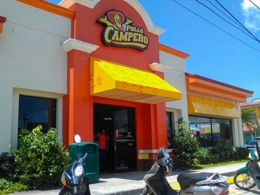 Fachada del restaurante El Campero con toldo naranja y amarillo, scooters aparcados fuera, bajo un cielo azul.