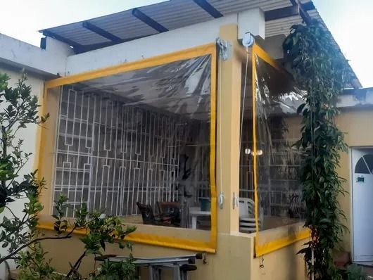 Cerramiento de esquina de vidrio con marco amarillo y rejas de seguridad metálicas bajo un techo de porche.