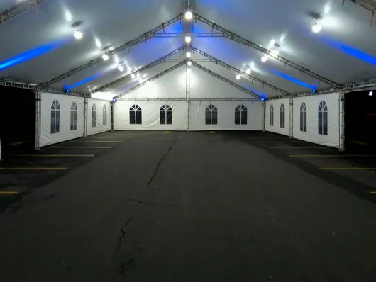 Carpa blanca vacía para eventos con luces azules y ventanas arqueadas sobre un suelo oscuro.
