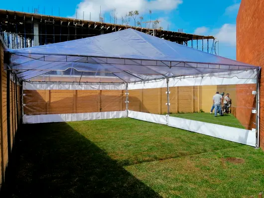 Una carpa blanca con toldo se encuentra en un patio cubierto de hierba, junto a una pared naranja.
