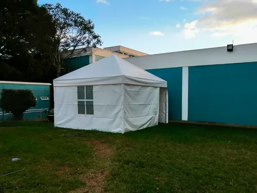 Carpa blanca para eventos en un patio con césped junto a un edificio color turquesa bajo un cielo azul.