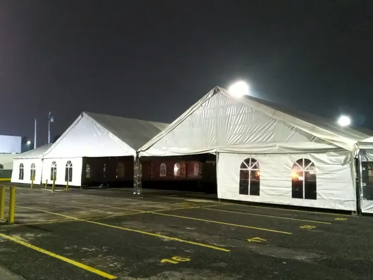 Carpas blancas para eventos iluminadas por la noche en un estacionamiento vacío.