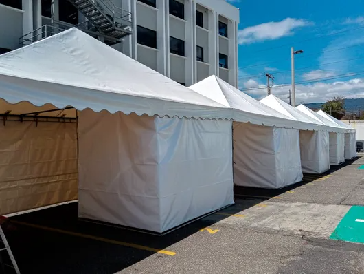 Carpas blancas para eventos se alineaban frente a un edificio en una calle soleada.