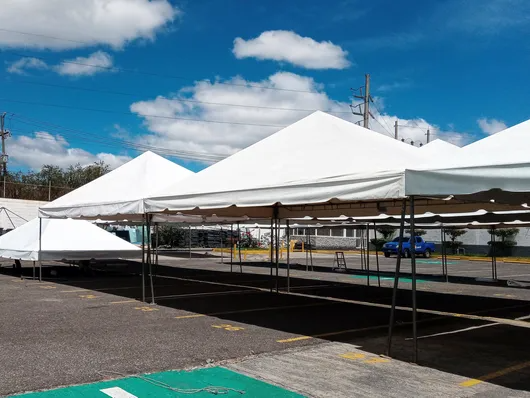 Carpas blancas para eventos instaladas en un terreno pavimentado bajo un cielo azul con nubes.